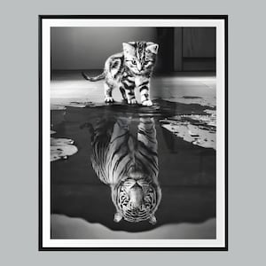 May include: Black and white framed print featuring a kitten standing in water, with its reflection showing a tiger. The kitten has black stripes and is looking forward. The tiger reflection is detailed with stripes.