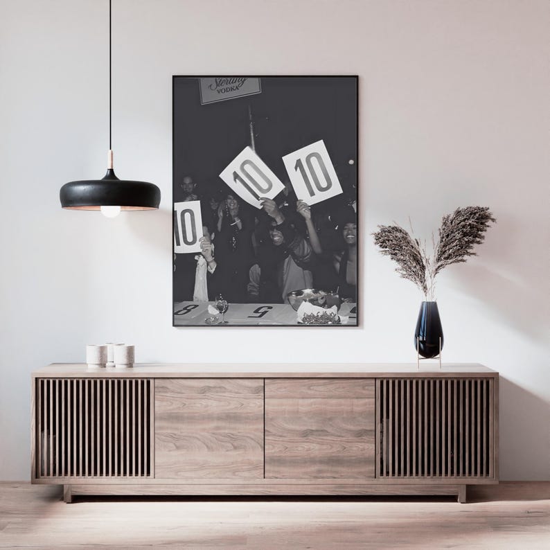 May include: Black and white framed photograph of a crowd holding up signs with the number 10. The photograph is hanging above a wooden cabinet with a black pendant light and a vase of dried plants.