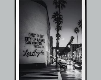 Peut inclure: Photographie en noir et blanc d'une rue de Los Angeles au crépuscule. L'image présente des palmiers, des voitures et un bâtiment avec le texte "ONLY IN THE CITY OF ANGELS CAN YOU FEEL THIS ALIVE" et "Los Angeles."