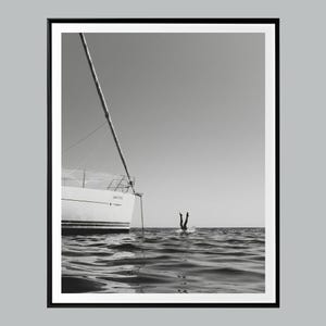 以下が含まれることがあります： モノクロ写真。ヨットと水中に飛び込む人の姿。白いヨットにはマストと索具があります。人が頭から水に飛び込み、足を上に伸ばしています。