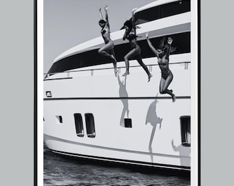 May include: Black and white photograph of three people jumping off a yacht into the water. The yacht is white with dark windows and a curved top. The people are wearing swimsuits and have their arms raised.
