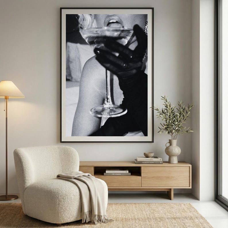 May include: Black and white framed art print. The image features a person holding a martini glass. The person is wearing long black gloves. The image is a close-up of the person's face and arm.