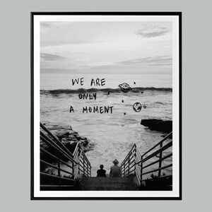 May include: Monochrome framed print showing a seascape with steps leading to the sea. The handwritten text "WE ARE ONLY A MOMENT" is above the water, with planet and star doodles. Two figures sit on the steps.