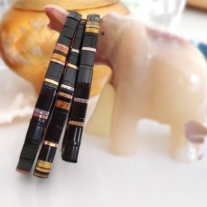 May include: Three black bracelets with gold, silver, and copper accents. The bracelets are stacked on top of each other.