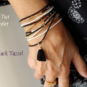 May include: A gold and black beaded bracelet with a black tassel. The bracelet is layered and has a gold accent. The text "Gold Tux Bracelet" and "Black Tassel" is visible in the image.