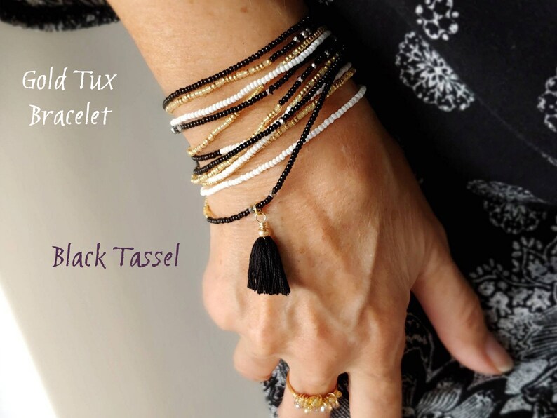 May include: A gold and black beaded bracelet with a black tassel. The bracelet is layered and has a gold accent. The text "Gold Tux Bracelet" and "Black Tassel" is visible in the image.