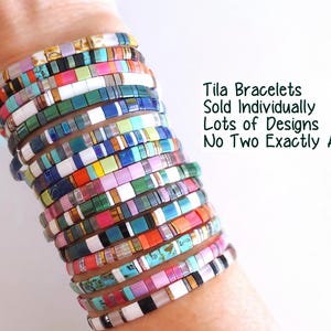 Peut inclure: Une pile de bracelets de perles Tila multicolores pr&eacute;sentant divers motifs et teintes, notamment rose, bleu, vert, blanc et des tons m&eacute;talliques. Le texte indique : Tila Bracelets Sold Individually Lots of Designs No Two Exactly Alike!