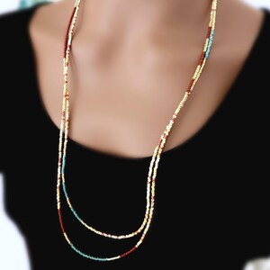 May include: A long, layered necklace with small, colourful beads. The necklace features a mix of colours, including gold, red, and turquoise. The beads are strung together to create a delicate and elegant accessory.