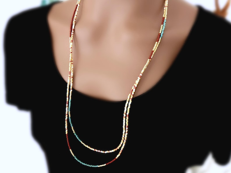 May include: A long, layered necklace with small, colourful beads. The necklace features a mix of colours, including gold, red, and turquoise. The beads are strung together to create a delicate and elegant accessory.