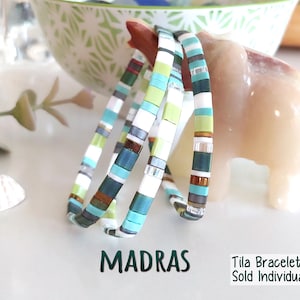 Peut inclure: Trois bracelets compos&eacute;s de perles carr&eacute;es et plates multicolores dans des tons de bleu sarcelle, vert lime, blanc et bronze m&eacute;tallique. Le texte MADRAS et Tila Bracelets Sold Individually est imprim&eacute; en vert fonc&eacute; sous les bracelets.