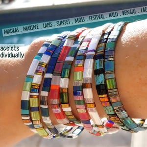 Peut inclure: Une collection de bracelets Tila compos&eacute;s de perles carr&eacute;es et plates dans diverses couleurs, dont le blanc, le bleu, le rouge, le vert et des finitions iris&eacute;es. Le texte indique MADRAS . MARINE . LAPIS . SUNSET . MOSS . FESTIVAL . HALO . BENGAL . LACQUER et Tila Bracelets Sold Individually.