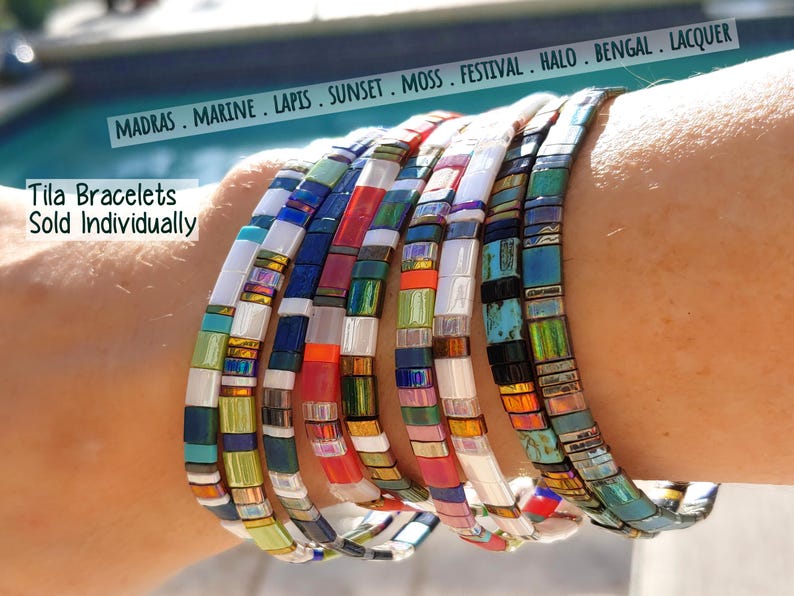 Peut inclure: Une collection de bracelets Tila compos&eacute;s de perles carr&eacute;es et plates dans diverses couleurs, dont le blanc, le bleu, le rouge, le vert et des finitions iris&eacute;es. Le texte indique MADRAS . MARINE . LAPIS . SUNSET . MOSS . FESTIVAL . HALO . BENGAL . LACQUER et Tila Bracelets Sold Individually.