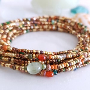 May include: A multi-strand beaded bracelet with gold, brown, orange, green, and clear beads. The bracelet features a large, light green gemstone.