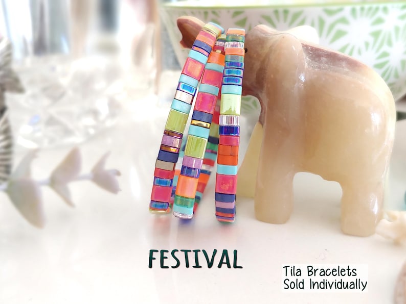 Peut inclure: Trois bracelets Tila empil&eacute;s compos&eacute;s de perles de verre carr&eacute;es multicolores dans des tons de rose, orange, bleu, vert et or m&eacute;tallique. Le texte FESTIVAL et Tila Bracelets Sold Individually est imprim&eacute; en noir au bas de l'image.