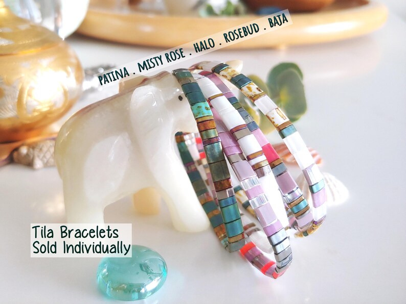 Peut inclure: Quatre bracelets Tila compos&eacute;s de perles carr&eacute;es dans des tons bleu sarcelle, bronze m&eacute;tallique, blanc, rose et lavande. Le texte PATINA . MISTY ROSE . HALO . ROSEBUD . BAJA et Tila Bracelets Sold Individually est visible sur l'image.