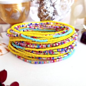 K&ouml;nnte beinhalten: Ein Stapel bunter Perlenarmb&auml;nder mit einer gelben Grundfarbe. Die Armb&auml;nder bestehen aus kleinen, runden Perlen in verschiedenen Farben, darunter Blau, Gr&uuml;n, Rosa und Rot.
