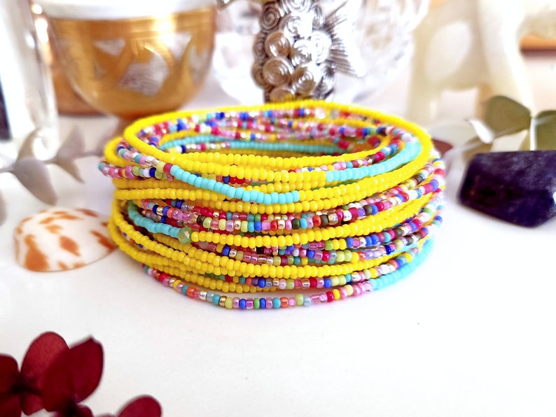 K&ouml;nnte beinhalten: Ein Stapel bunter Perlenarmb&auml;nder mit einer gelben Grundfarbe. Die Armb&auml;nder bestehen aus kleinen, runden Perlen in verschiedenen Farben, darunter Blau, Gr&uuml;n, Rosa und Rot.