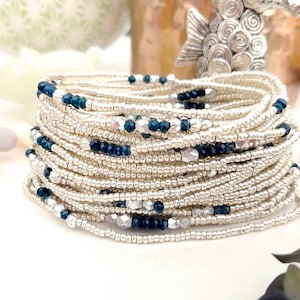 May include: A stack of silver and blue beaded bracelets. The bracelets are made with small, round beads and feature a mix of silver and dark blue beads.