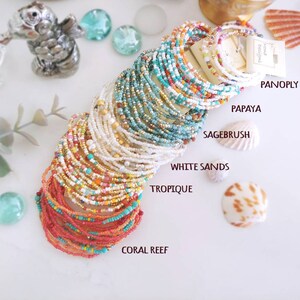 K&ouml;nnte beinhalten: Ein Stapel bunter Perlenarmb&auml;nder mit Namen wie "Coral Reef", "Tropique", "White Sands", "Sagebrush", "Papaya" und "Panoply Pearl".