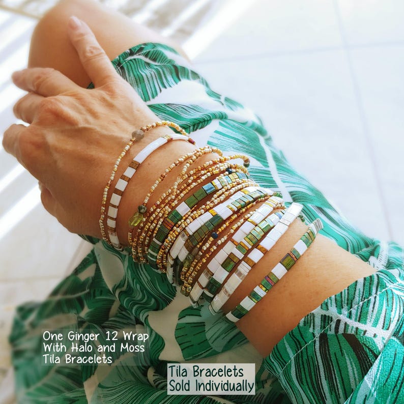 Peut inclure: Une collection de bracelets Tila avec des carreaux carr&eacute;s blancs, vert mousse et or m&eacute;tallique, ainsi que des brins de perles d&eacute;licats. Le texte indique : One Ginger 12 Wrap With Halo and Moss Tila Bracelets. Tila Bracelets Sold Individually.