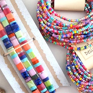 Peut inclure: Trois bracelets de perles carr&eacute;es Tila multicolores sur une carte et deux bracelets multi-tours de perles de rocaille multicolores avec des &eacute;tiquettes Nona Designs. Le texte indique : 3 Festival Tila Bracelets, Two 12-wrap Trapeze Bracelets, Tila Bracelets Sold Individually.