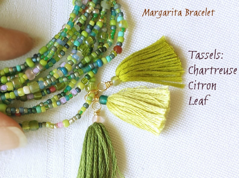 May include: A multi-strand beaded bracelet with green, blue, and white beads. The bracelet has three tassels attached to it, in the colors chartreuse, citron, and leaf. The text "Margarita Bracelet" and "Tassels: Chartreuse Citron Leaf" is visible in the image.
