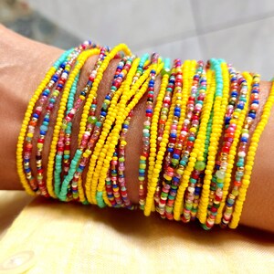 K&ouml;nnte beinhalten: Ein farbenfrohes Perlenarmband mit mehreren Reihen gelber, blauer, gr&uuml;ner, roter und rosa Perlen. Das Armband ist um das Handgelenk einer Person gewickelt.