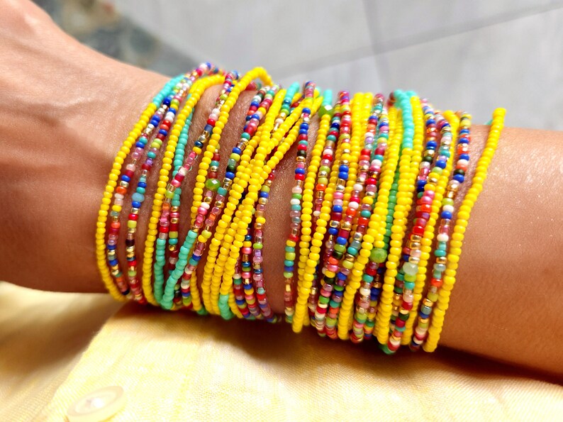 K&ouml;nnte beinhalten: Ein farbenfrohes Perlenarmband mit mehreren Reihen gelber, blauer, gr&uuml;ner, roter und rosa Perlen. Das Armband ist um das Handgelenk einer Person gewickelt.