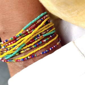 K&ouml;nnte beinhalten: Ein farbenfrohes Armband mit mehreren Reihen gelber, roter, blauer, gr&uuml;ner und wei&szlig;er Perlen.