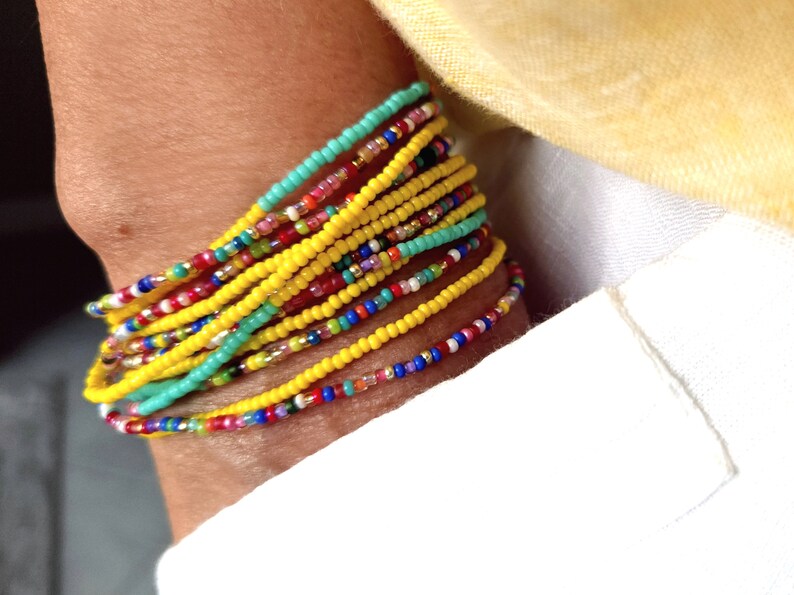 K&ouml;nnte beinhalten: Ein farbenfrohes Armband mit mehreren Reihen gelber, roter, blauer, gr&uuml;ner und wei&szlig;er Perlen.