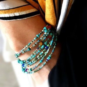 May include: A stack of colorful beaded bracelets in shades of turquoise, blue, green, and brown. The bracelets are made of small, round beads and are layered on top of each other.