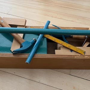 Peut inclure: Une boîte à outils en bois remplie d'outils, dont un marteau, une règle, une scie et un tournevis. La boîte à outils est peinte en bleu et possède une poignée en métal.
