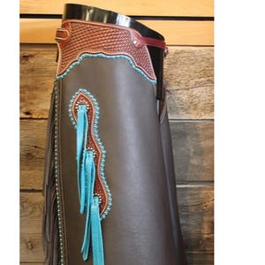 May include: Brown leather chaps with turquoise fringe and beading. The chaps have a brown leather belt with a silver buckle.