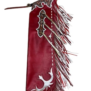 Op de afbeelding: Rode leren chaps met witte en zilveren franjes en versieringen. De chaps hebben een riemlus en een zilveren gesp.