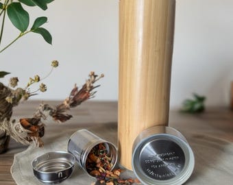 May include: A bamboo and stainless steel tea infuser bottle with a removable stainless steel infuser. The bottle has a bamboo exterior and a stainless steel interior. The infuser is filled with loose leaf tea. The bottle is sitting on a wooden surface.