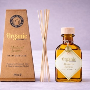 May include: A Madurai Jasmine reed diffuser set. The set includes a brown cardboard box with gold text, a glass bottle with a wooden cap, and a bundle of reeds. The bottle contains a golden liquid and has a label that reads "Organic Goodness".