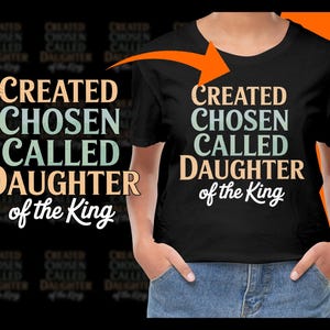 Può includere: Una maglietta nera con il testo "CREATED CHOSEN CALLED DAUGHTER of the King" in un font in stile vintage. Il testo è in tonalità di blu, verde e arancione.