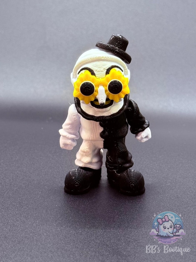 May include: A 3D-printed figurine of a whimsical character, split vertically with white and black halves. It wears a black top hat and yellow gear-shaped glasses. The figure has a white face, a black mustache, and large black shoes.