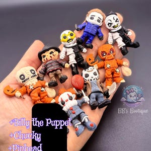 May include: A collection of miniature horror movie character figurines, including Michael Myers, Jason Voorhees, and others. The figures are brightly colored and detailed, with a variety of costumes and accessories. The figurines are held in a hand.