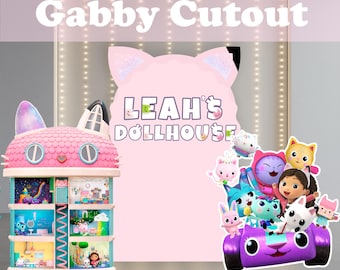 Puede incluir: Un recorte rosa de Gabby's Dollhouse con el texto "Gabby Cutout" en la parte superior. La imagen presenta un recorte rosa con forma de gato con el texto "LEAH'S DOLLHOUSE". También se ven una casa de muñecas y un coche morado con personajes.