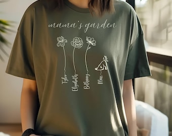 Può includere: Una maglietta verde con il testo "mama's garden" e un disegno floreale con i nomi "Tyler", "Elizabeth", "Bethany" e "Max" sotto.