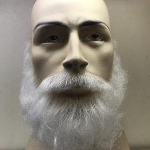 Könnte beinhalten: Ein Schaufensterpuppenkopf mit einem realistischen Gesicht und einem vollen, flauschigen weißen Bart und Schnurrbart. Der Kopf ist hellbeige, mit bemalten Augenbrauen und realistischen Augen. Der Bart und Schnurrbart bestehen aus weichem, weißem Material.