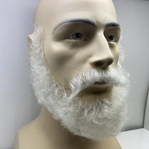 May include: A white fake beard and moustache on a mannequin head. The beard is long and full, and the moustache is thick and bushy.