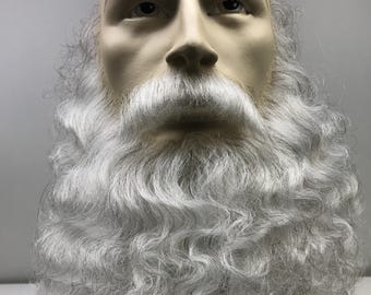 May include: A mannequin head with a bald scalp, realistic facial features, and a long, white, curly beard and mustache. The face has a neutral expression, and the beard is full and voluminous, suggesting a costume or theatrical prop.