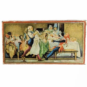 May include: A rectangular box with a colorful illustration of a medieval banquet scene. The image depicts several figures in period clothing, including a jester, gathered around a table laden with food. The artwork has a vintage aesthetic with a red border.