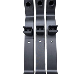 Puede incluir: Tres soportes verticales negros. Cada soporte tiene una parte superior rectangular con una abertura circular, una sección media con un soporte rectangular más pequeño y una base con dos orificios para el montaje. Los soportes están hechos de un material negro mate.