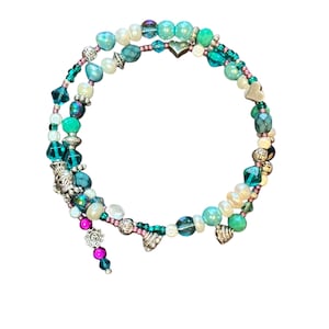 Op de afbeelding: Een multi-strand wikkelarmband met kralen in tinten van teal, turquoise, wit en roze. De armband heeft zilverkleurige metalen accenten en hartvormige bedels. Een cluster van roze en teal kralen bungelt aan de armband.