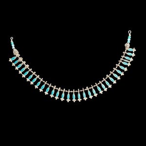 Puede incluir: Un collar plateado con detalles turquesa en forma de lágrima. El collar tiene un diseño delicado con pequeñas cuentas redondas en los extremos. El fondo es negro liso, resaltando la joya.