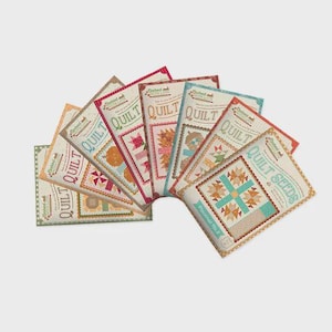 May include: A collection of colorful quilt pattern packets fanned out on a light background. Each packet features a different quilt design, with text that reads "QUILT" and "Baked with Love". The packets showcase various geometric and floral patterns.