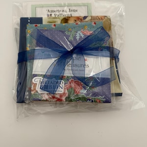 K&ouml;nnte beinhalten: Ein Stoffb&uuml;ndel, verpackt in durchsichtigem Zellophan und mit einem dunkelblauen Band gebunden. Das B&uuml;ndel enth&auml;lt Stoffquadrate mit Blumen- und Tupfenmustern sowie eine Karte mit der Aufschrift "American Jane Patterns" und "Simple Measures".